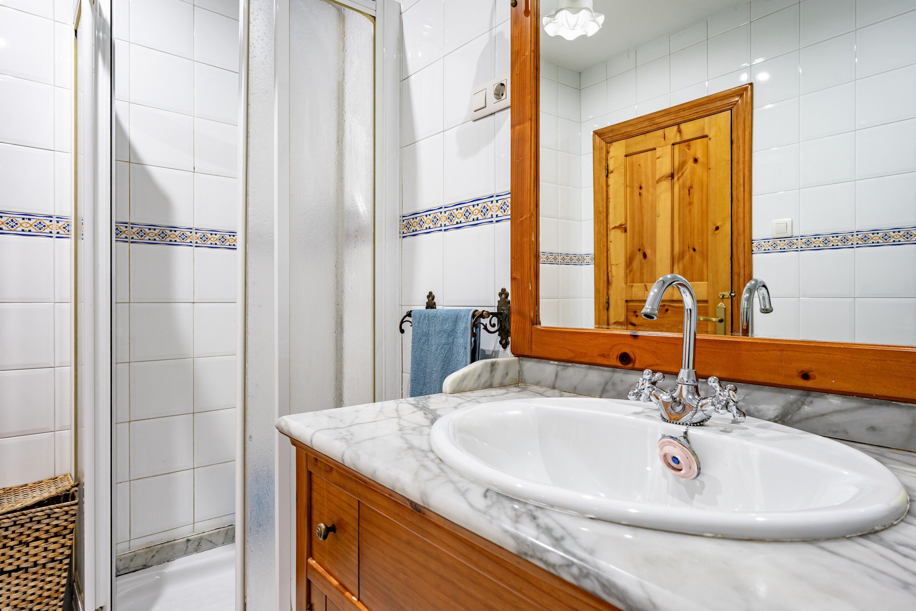 A bathroom with a marble sink, wooden vanity, and a mirror reflecting a wooden door.