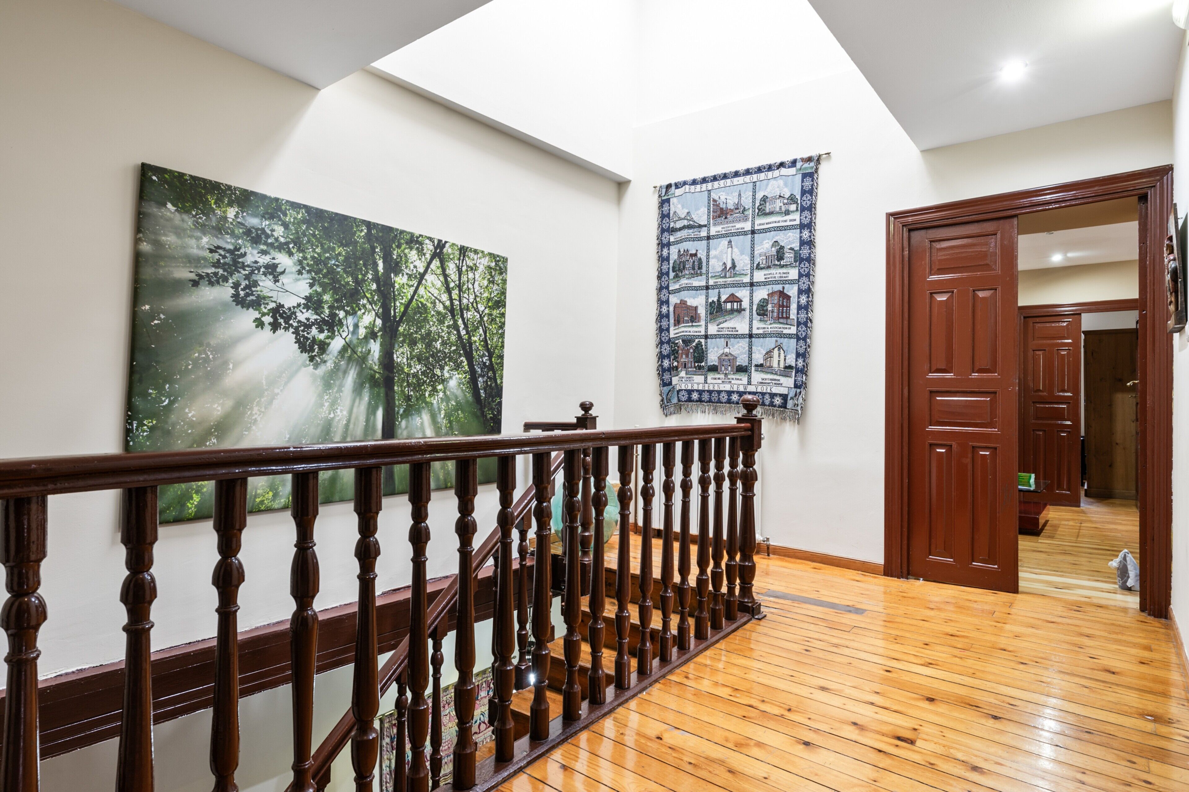 A wooden staircase with a railing, a large painting of a forest, and a wall tapestry.