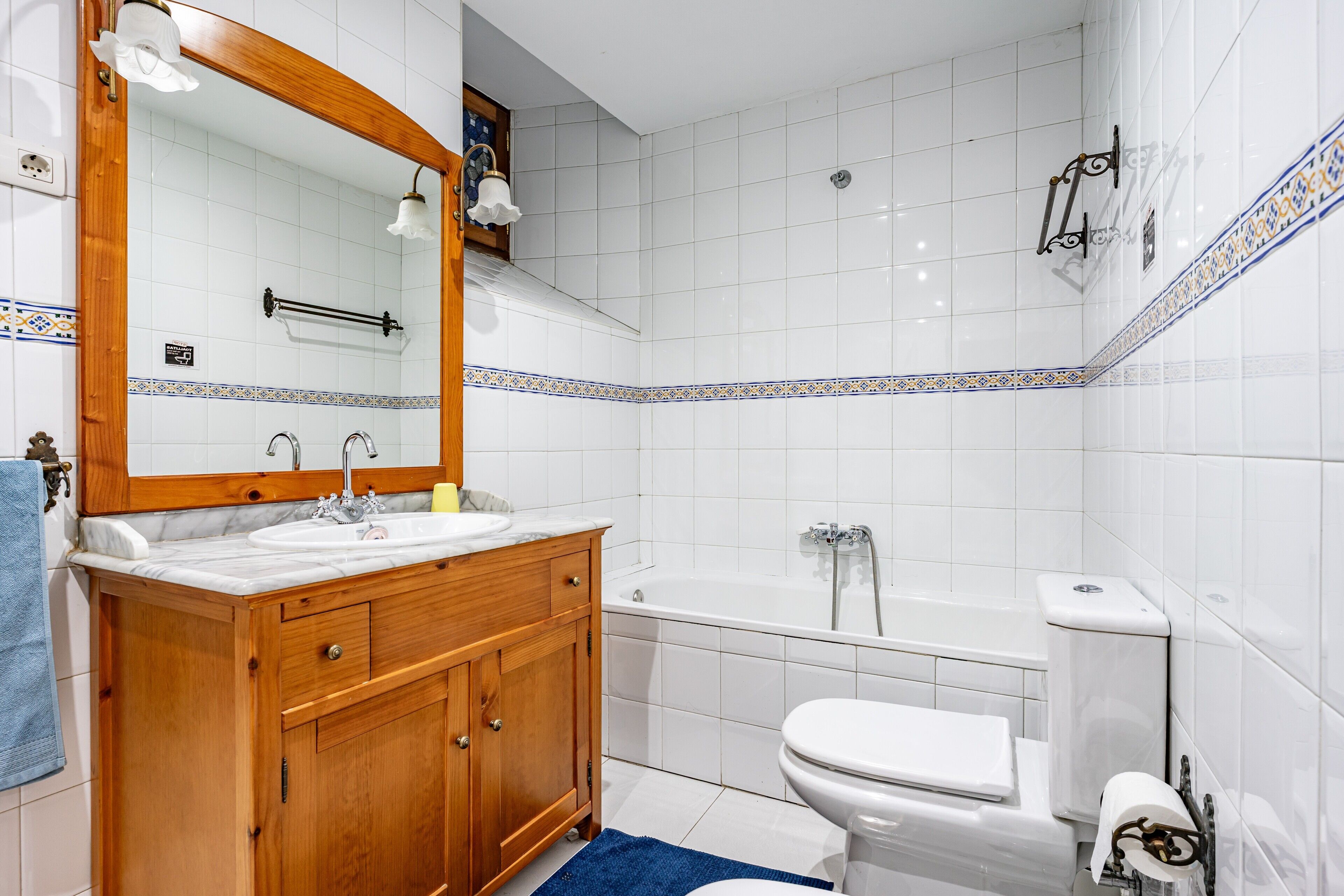 Ein Badezimmer mit einem Holzkosmetikschrank, einem weißen Waschbecken, einem Spiegel, einer Badewanne und einer Toilette.