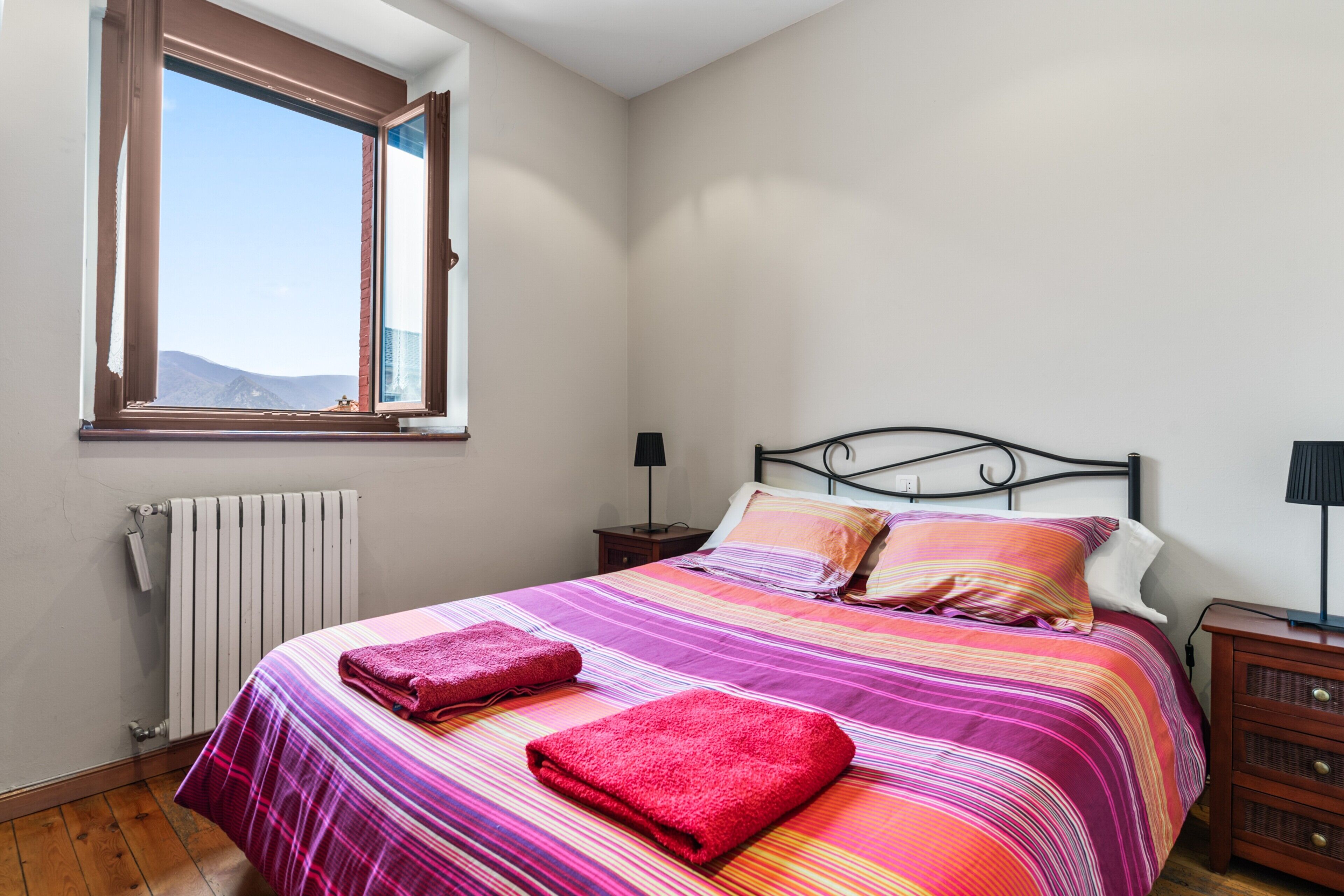 Un dormitorio con cama, ventana, radiador, mesita de noche y cómoda.