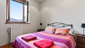 Un dormitorio con cama, ventana, radiador, mesita de noche y cómoda.