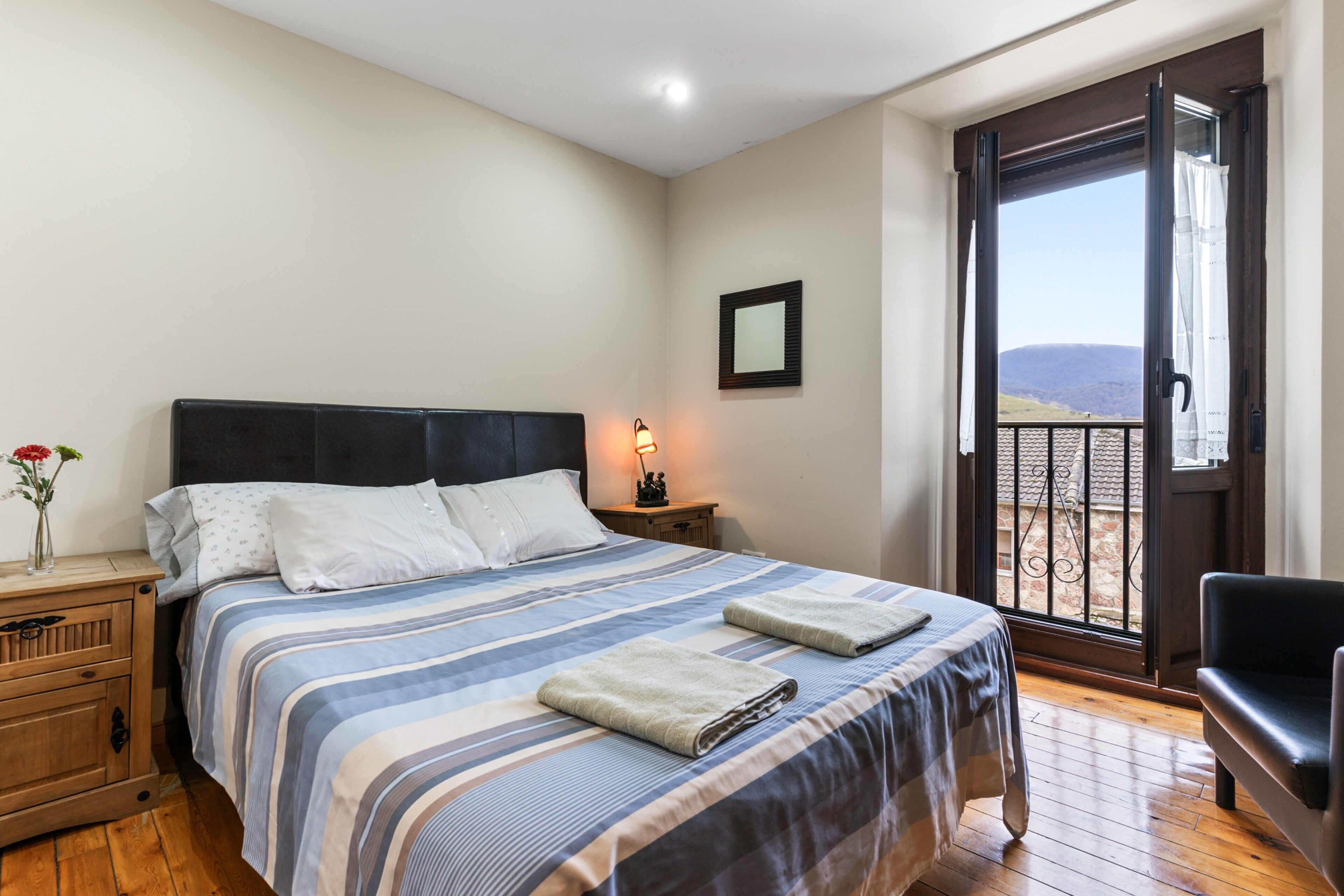 Een slaapkamer met een bed, nachtkastje, lamp en uitzicht door een balkondeur.