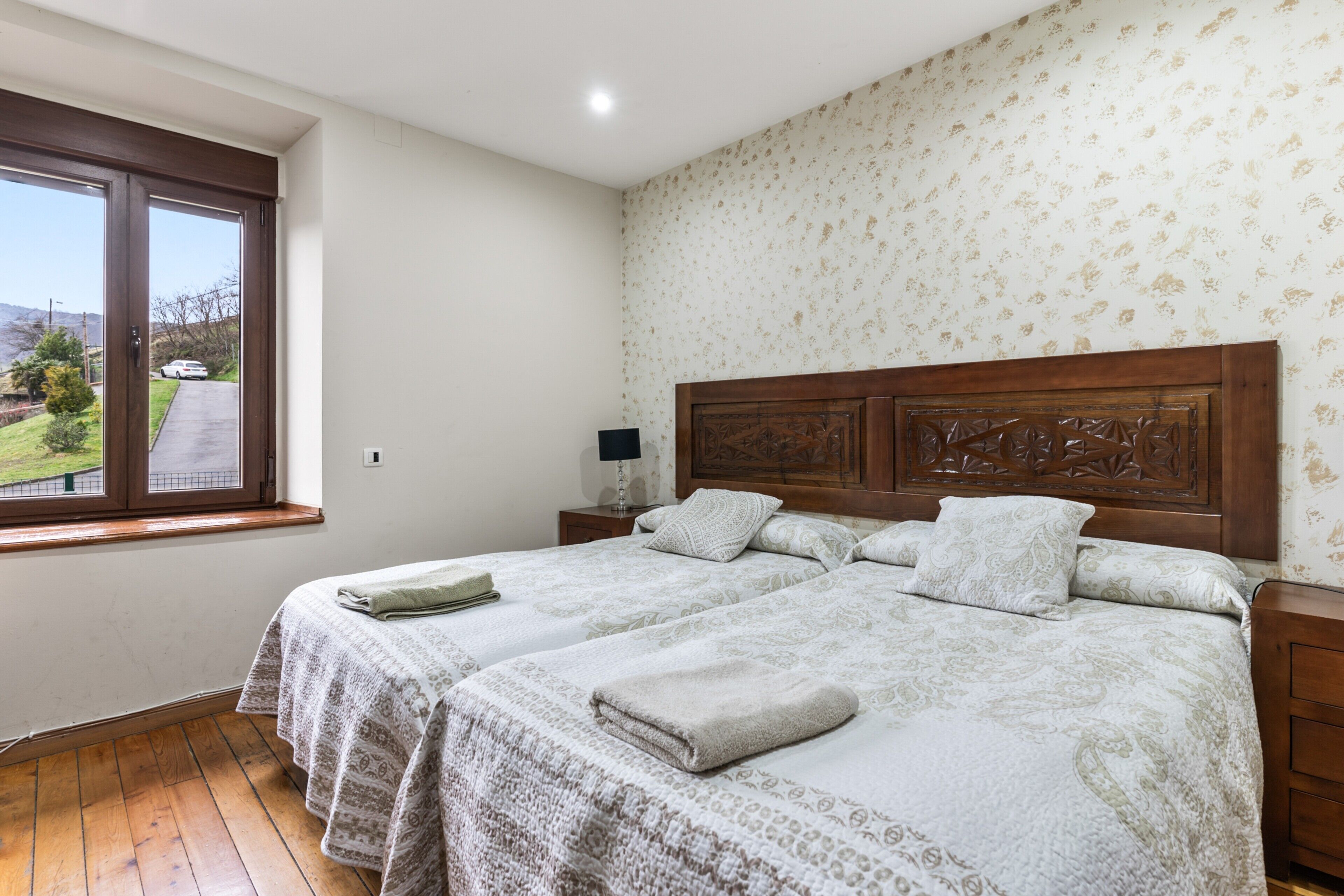 Une chambre avec deux lits, une fenêtre donnant sur un beau paysage, une tête de lit en bois et une table de chevet avec une lampe.