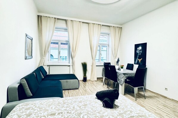 Una habitación moderna con una cama, un sofá, una mesa de comedor con sillas y un ventanal con cortinas.