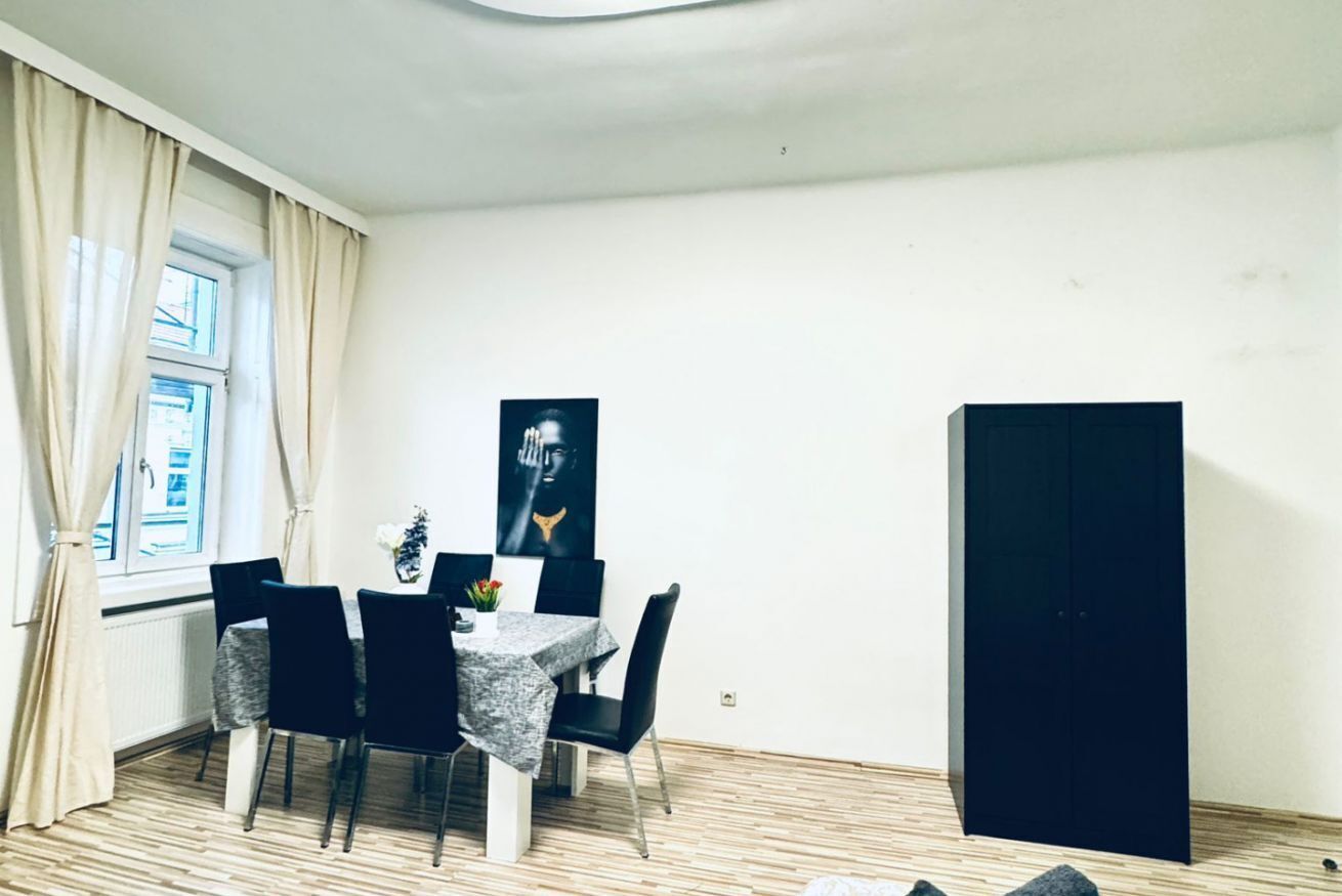 Un coin repas comprenant une table, des chaises, un meuble noir et une fenêtre avec des rideaux.