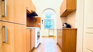 A narrow kitchen with wooden cabinets, a window, and a door leading to another room. - Affordable 2BR Apartment; Close to Danube River (Vienna)