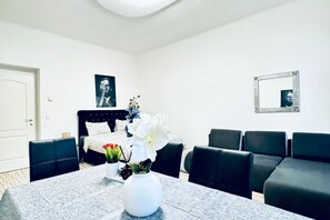 Habitación de hotel con una mesa de comedor, sillas, una cama con cabecero, un espejo y un cuadro en la pared.