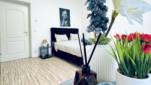 A bedroom with a bed, a white door, a bedside table, a wall art piece, and a potted plant. - Affordable 2BR Apartment; Close to Danube River (Vienna)
