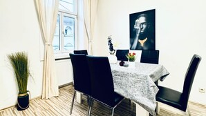 A dining area with a table set for two, black chairs, a vase with flowers, and a large black and white artwork on the wall. - Affordable 2BR Apartment; Close to Danube River (Vienna)