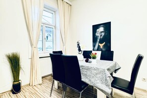 A dining area with a table set for two, black chairs, a vase with flowers, and a large black and white artwork on the wall.