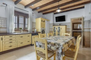 Una cocina con una mesa de comedor, sillas, un televisor y una ventana con cortinas.