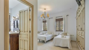 Een slaapkamer met twee bedden, een kroonluchter, een kledingkast en een badkamer met een spiegel en wastafel.