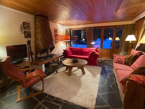 Un salón acogedor con suelo de piedra, chimenea, sofá rojo y televisor.