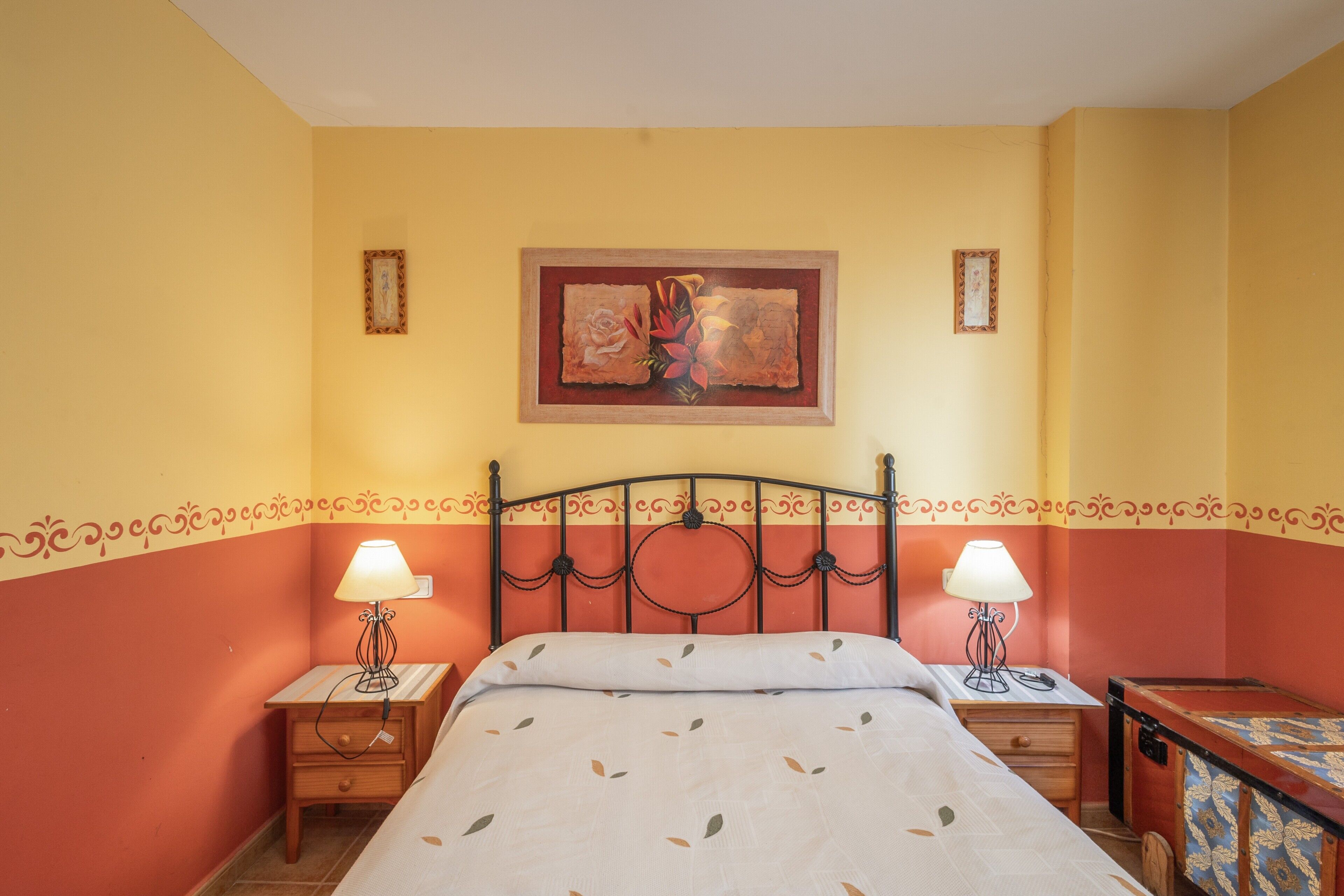 Ein Hotelzimmer mit einem Bett, zwei Nachttischen, einer Lampe, einem gerahmten Bild an der Wand und einem Koffer.
