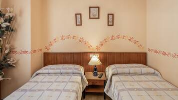 Habitación de hotel con dos camas, una mesita de noche con lámpara y tres cuadros enmarcados en la pared.