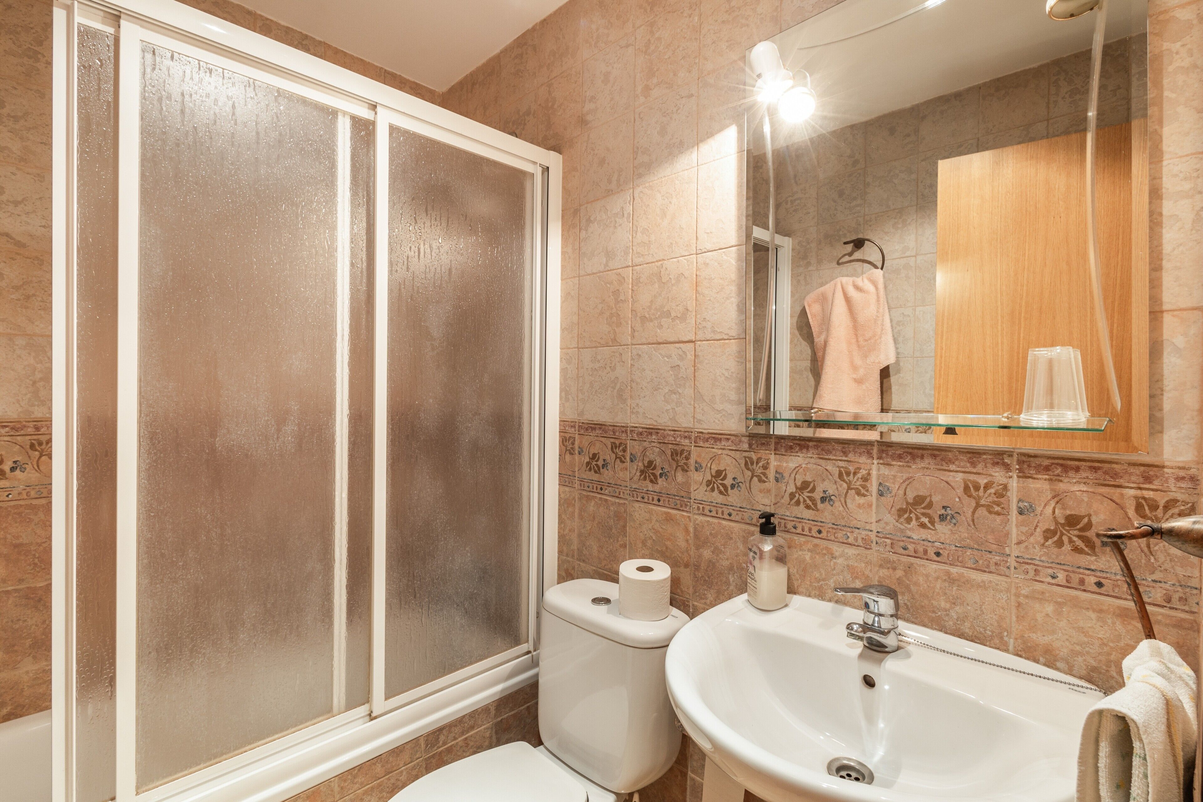 A bathroom with a shower, toilet, sink, and a mirror.