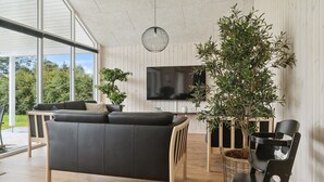 Una sala de estar moderna con un sofá de cuero negro, piso de madera, un televisor grande y un árbol en maceta.
