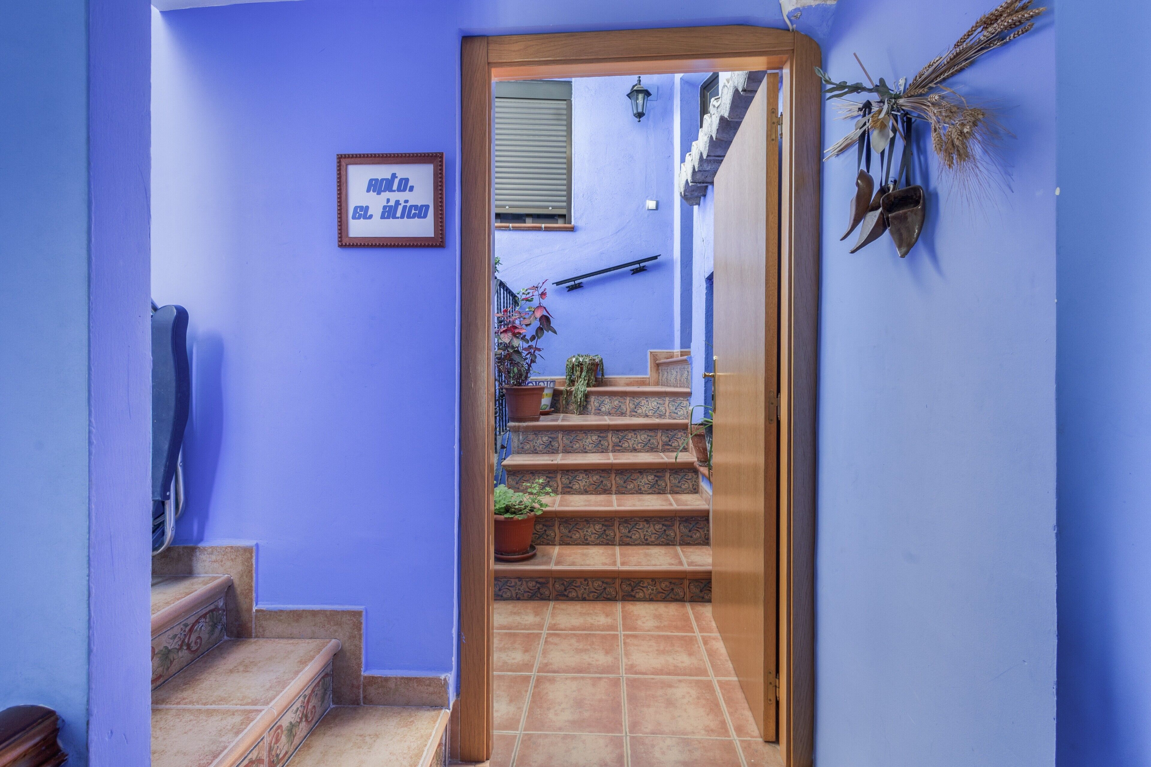 Un couloir aux murs bleus, une porte en bois et un escalier menant à un balcon.