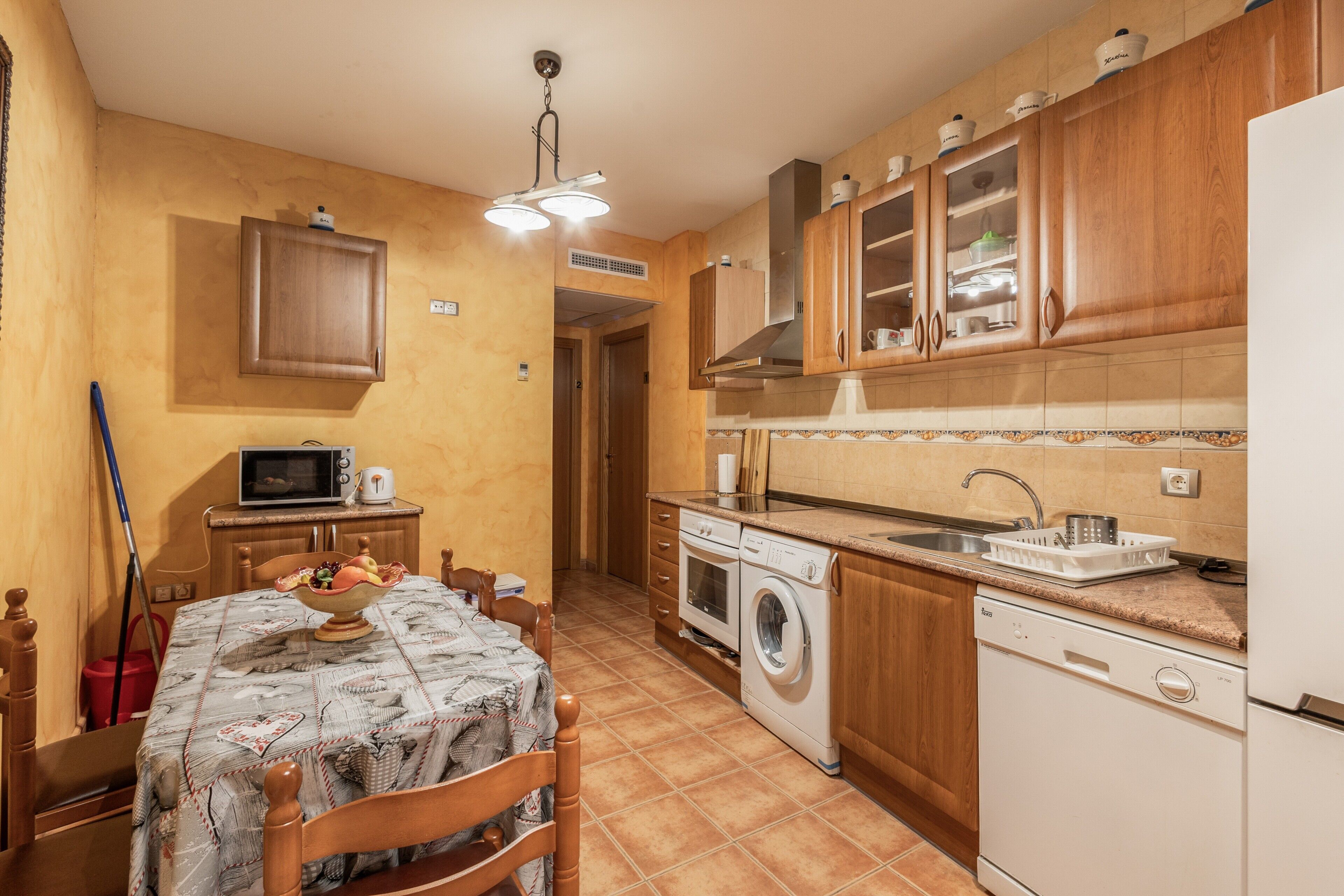 Une cuisine avec des meubles de rangement en bois, un four à micro-ondes, un lave-linge et une table à manger avec des chaises.