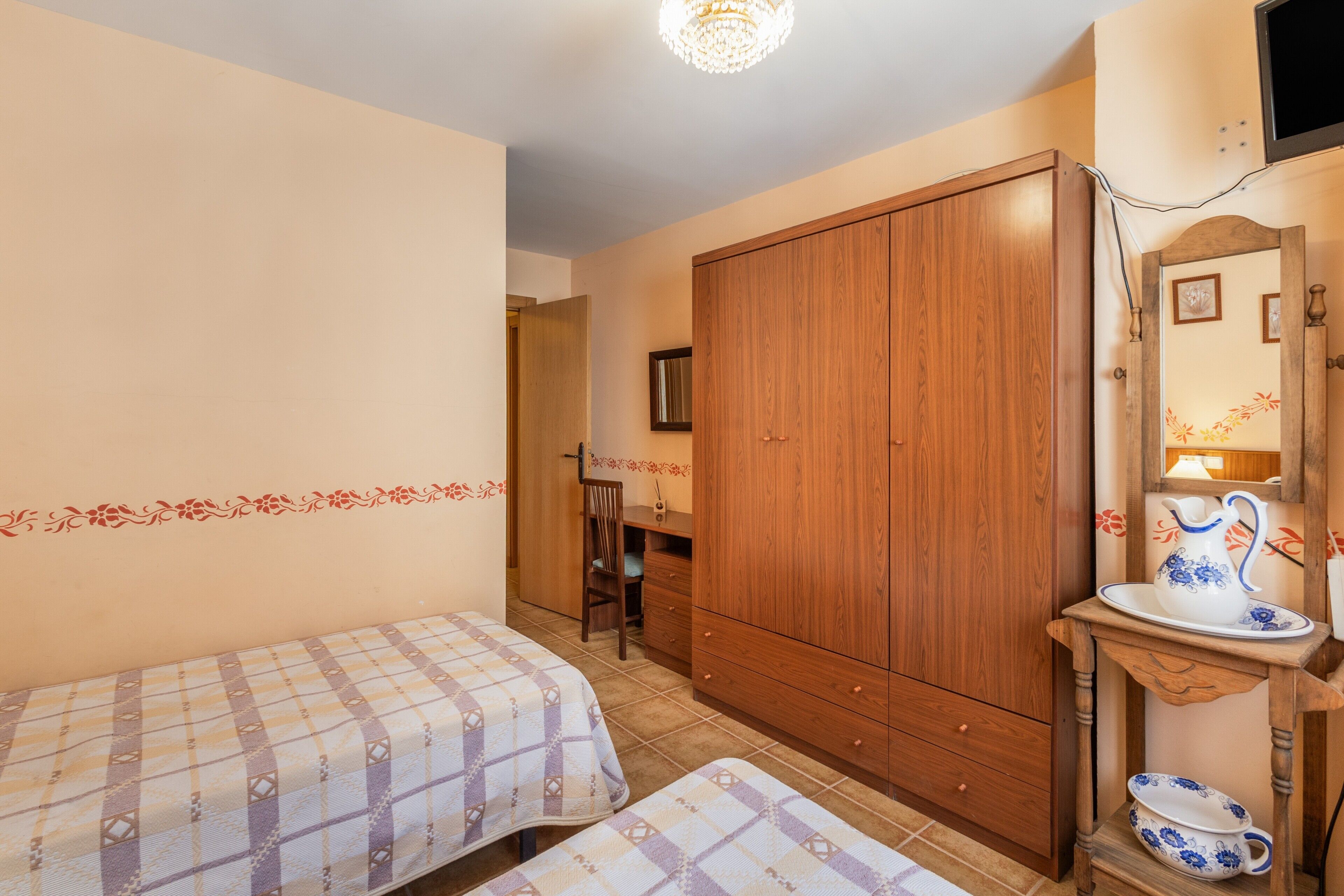 Een slaapkamer met twee bedden, een houten garderobe, een klein tafeltje met een karaf en een spiegel.