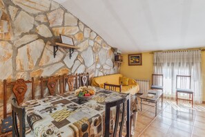 A dining area with a stone wall, wooden chairs, a table with a patterned tablecloth, and a yellow sofa.