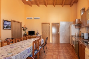 Una cocina compacta con armarios de madera, una mesa de comedor con sillas, un televisor y un refrigerador.