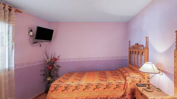 Une chambre à coucher avec un lit, une table de chevet avec une lampe, un téléviseur fixé au mur et un vase rempli de fleurs.
