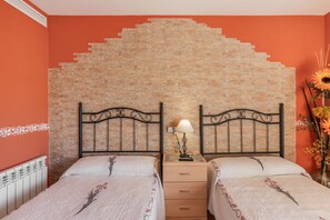 Quarto com duas camas, parede de tijolos, radiador e mesa de cabeceira com abajur.