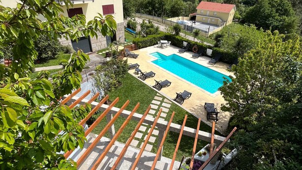 Una piscina con sillas de descanso, una pérgola y vistas a una ladera boscosa.
