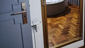 Una habitación con un espejo grande y ornamentado, una cama con ropa de cama blanca, una mesita de noche y una lámpara moderna.