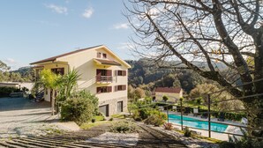 Un edificio de dos pisos con un balcón, una piscina y vistas de las colinas circundantes.