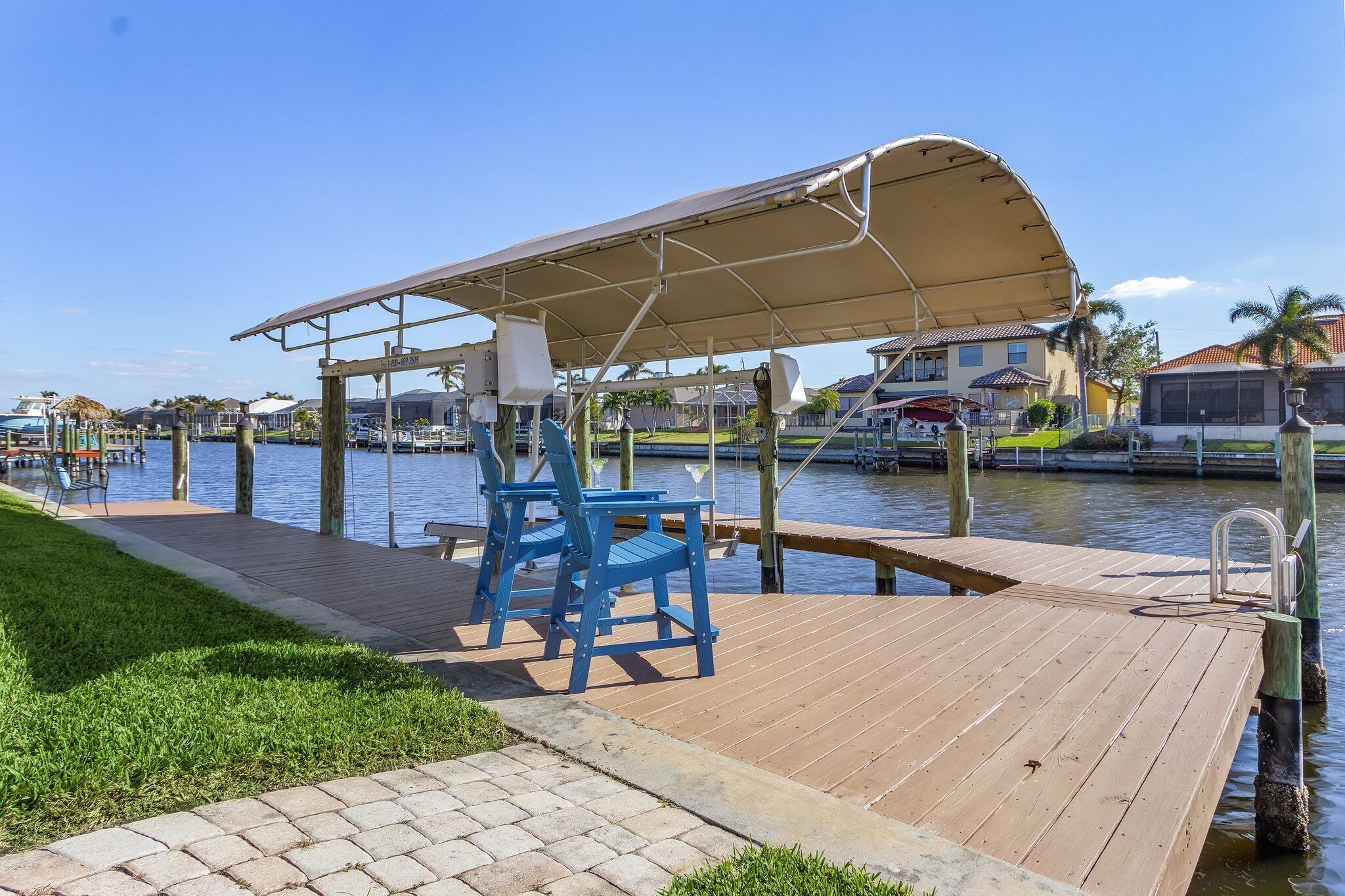 Un molo di legno con un’area salotto coperta e sedie, affacciato su uno specchio d’acqua con barche e case sullo sfondo.