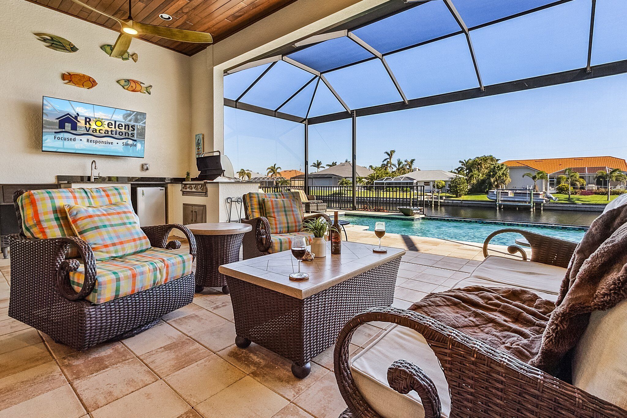 Amplio espacio interior con mobiliario de mimbre, un ventanal con vistas a una piscina y un cartel de Roelens Vacations.
