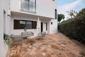 A modern outdoor patio with a brick floor, two grey sofas, a small round table, and a white umbrella. - Pear Tree Holiday Home with Private Terrace, Wi-Fi, and Air Conditioning (Vale de Lobo)