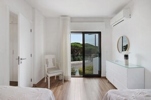 Een moderne hotelkamer met een bed, een stoel, een dressoir en een glazen schuifdeur die uitkomt op een balkon met uitzicht op groen.