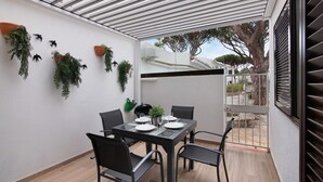 Uma área de refeições ao ar livre com mesa posta para quatro pessoas, rodeada por cadeiras e plantas em vasos na parede.