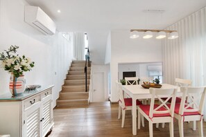 A modern kitchen with white cabinetry, a wooden staircase, and a dining area with white chairs and red cushions. - Pear Tree Holiday Home with Private Terrace, Wi-Fi, and Air Conditioning (Vale de Lobo)