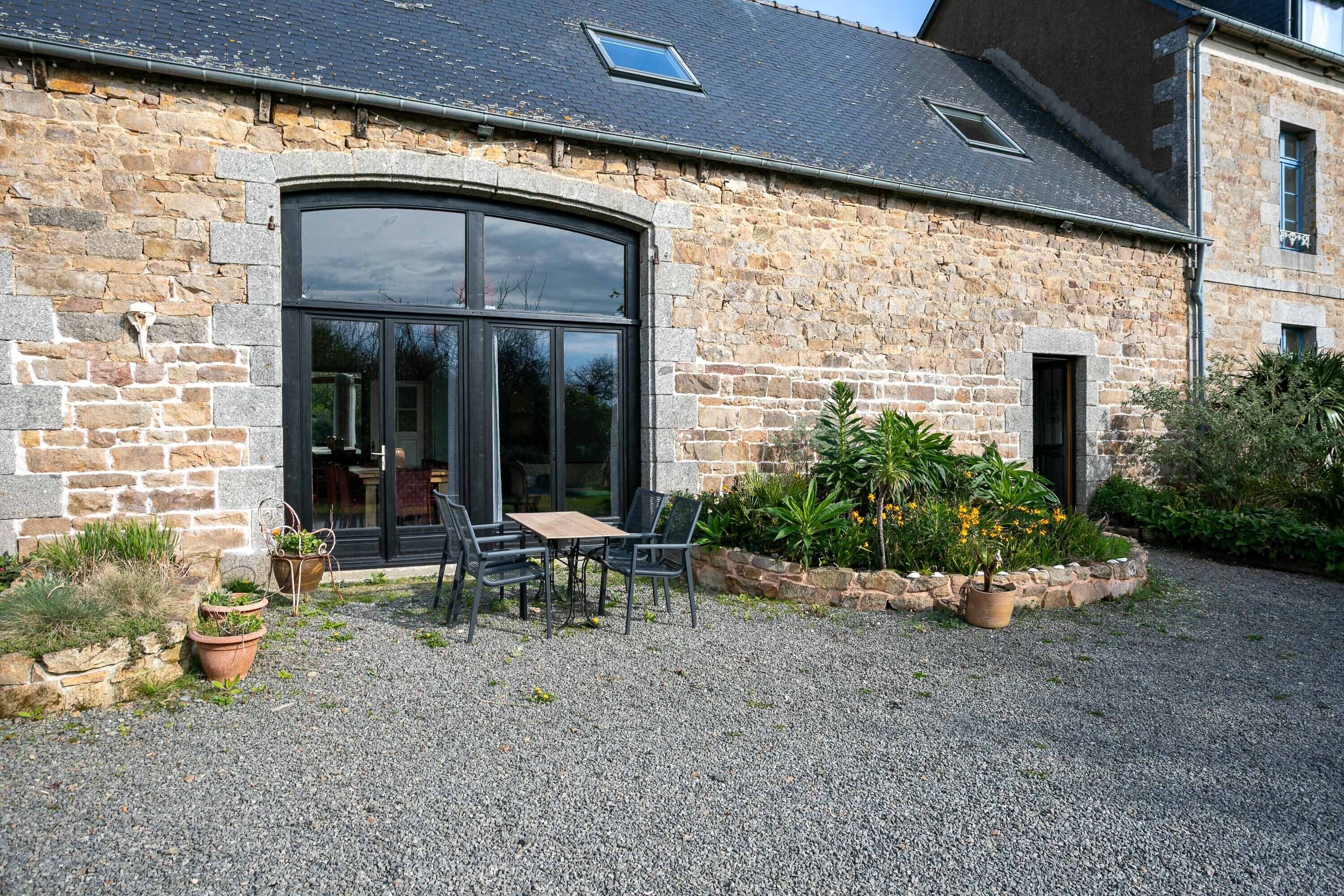 A stone building with a large arched window, outdoor seating, and potted plants.