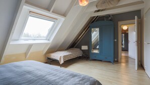 A bedroom with a sloped ceiling, a bed, a wardrobe, and a window. - Holiday Home 'Gite La Grange 6 Personnes' with Shared Pool, Private Terrace and Wi-Fi (Prat)