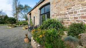 A stone building with a gravel driveway, potted plants, and a bench. - Holiday Home 'Gite La Grange 6 Personnes' with Shared Pool, Private Terrace and Wi-Fi (Prat)