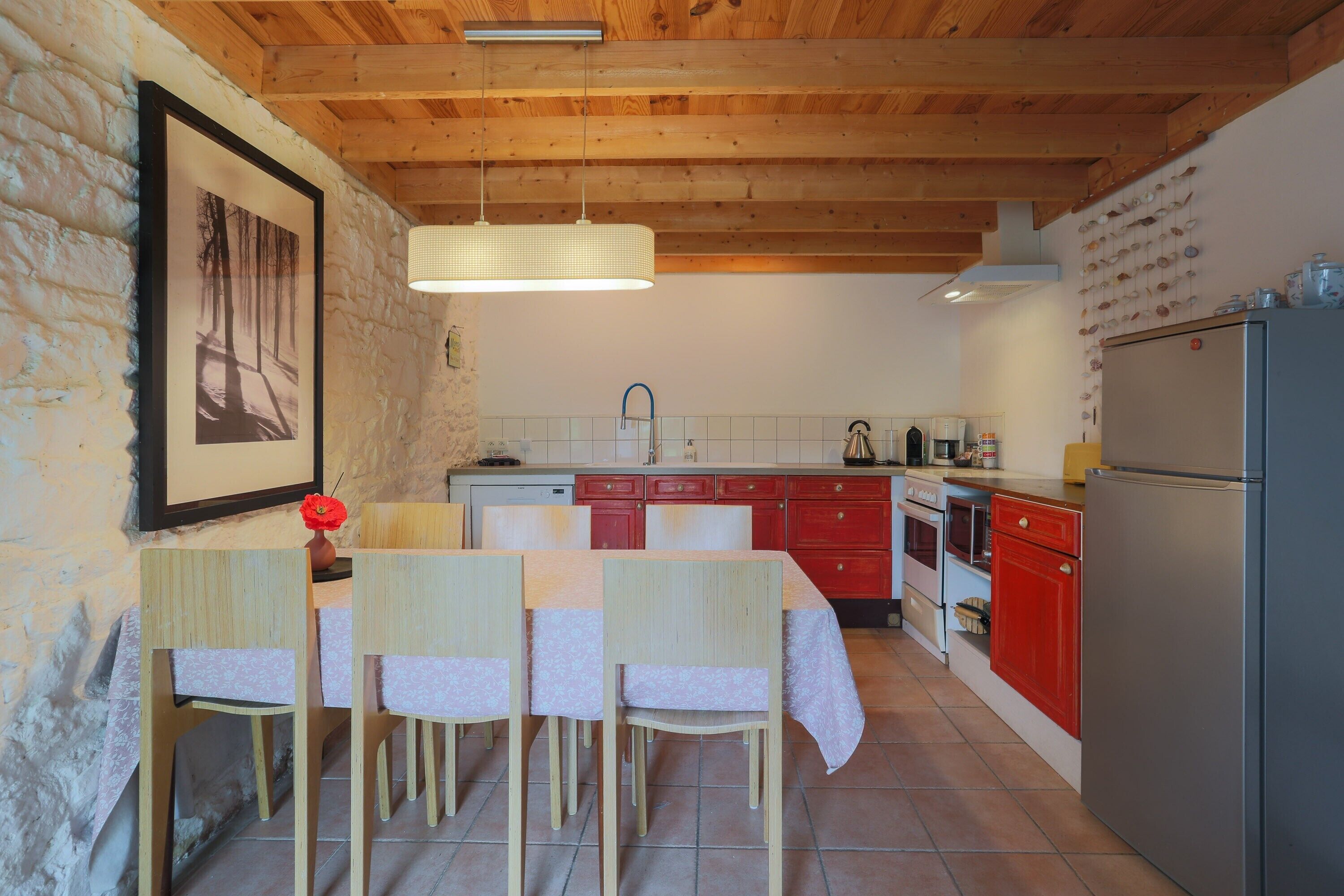 A kitchen with wooden beams, a dining table with chairs, a refrigerator, and a sink.