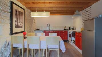 A kitchen with wooden beams, a dining table with chairs, a refrigerator, and a sink.