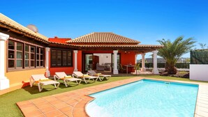 Une maison avec une piscine, un espace salon extérieur et une terrasse couverte.