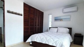 A bedroom with a bed, a wooden wardrobe, a nightstand, and an air conditioning unit. - Ocean view villa walking distance to restaurants, public beach and more (Dorado)