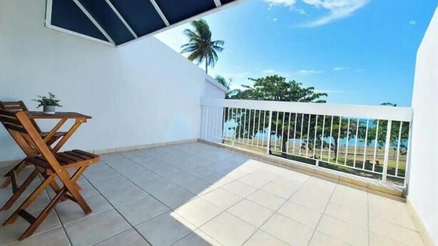 A balcony with a tiled floor, a wooden chair, a small table with a plant, and a white railing. - Ocean view villa walking distance to restaurants, public beach and more (Dorado)