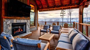 Una cabaña acogedora con chimenea de piedra, terraza de madera y vistas a la montaña.