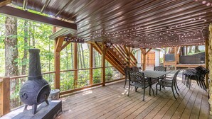 A covered deck with a wood-burning stove, a table with chairs, and a TV.