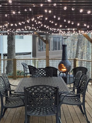 Eine Terrasseneinrichtung mit Tisch, Stühlen, einem Kaminofen und Lichterketten.