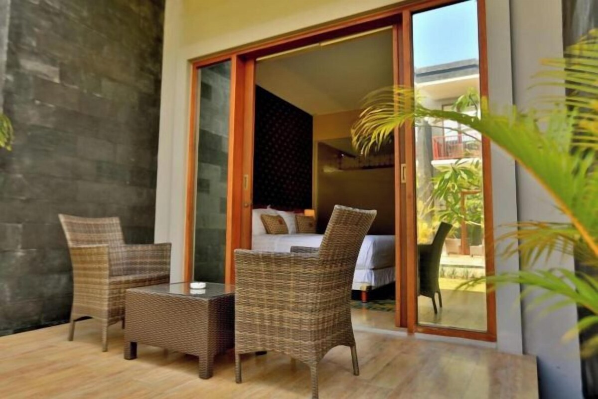 A room with a sliding glass door leading to a balcony, wicker furniture, and a bed with pillows.