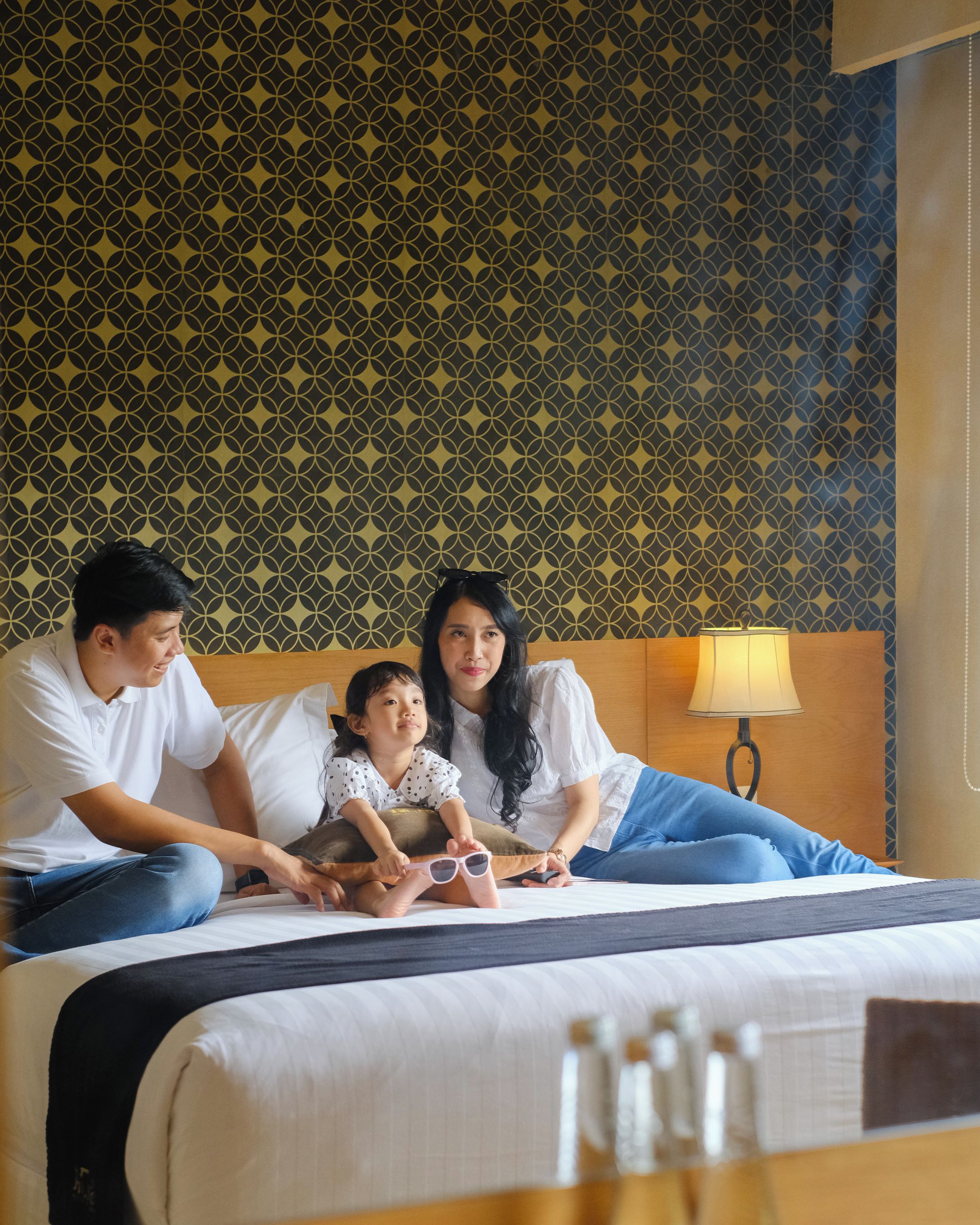 Una habitación de hotel con papel tapiz estampado, una cama con ropa blanca y una lámpara de noche.